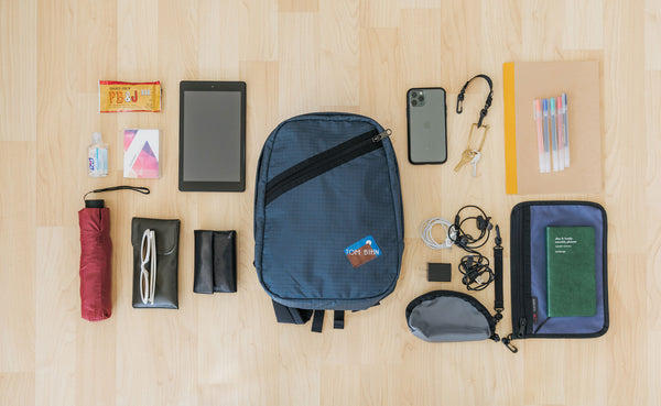 A possible pack for the Zeitgiest, including a retractable umbrella, sunglasses, Small Q-Kit with charge cords, a phone, keys, pens, a tablet, tissues and hand sanitizer, and a small Clear Organizer Pouch with a journal.
